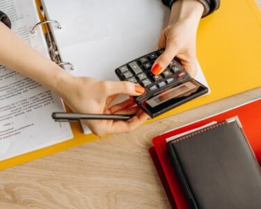 Hands using a calculator at a desk with documents and folders, ideal for finance or accounting themes.